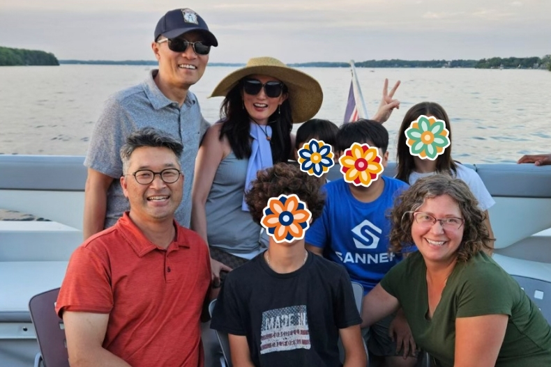 A group of adults and children sit together on a boat during a sunny day on the lake. The adults smile warmly toward the camera, while the children’s faces are covered with colorful flower stickers. A woman wearing a wide sunhat and sunglasses stands in the back, and the lake and shoreline stretch out behind them. The mood is relaxed, cheerful, and summery as everyone enjoys time together on the water.A group of adults and children sit together on a boat during a sunny day on the lake. The adults smile warmly toward the camera, while the children’s faces are covered with colorful flower stickers. A woman wearing a wide sunhat and sunglasses stands in the back, and the lake and shoreline stretch out behind them. The mood is relaxed, cheerful, and summery as everyone enjoys time together on the water.