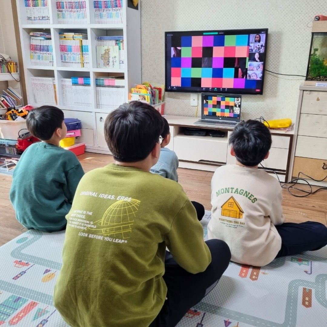 Children participating in a virtual KKOOM English camp looking at the tv monitor.