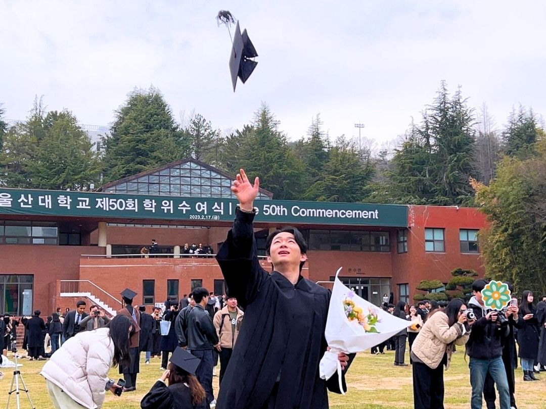 Student celebrating graduation outdoors while wearing a cap and gown.