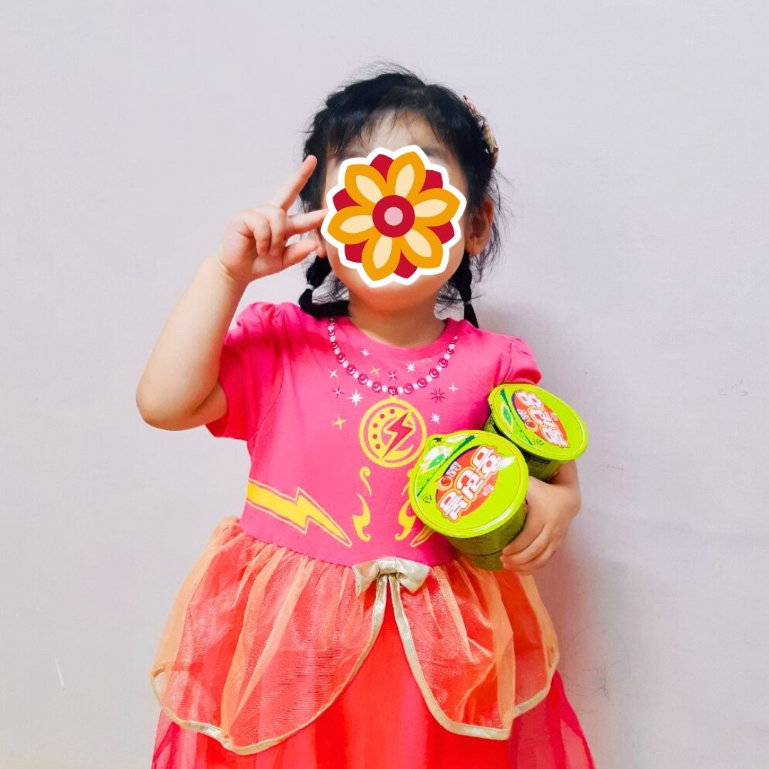 Child wearing a colorful outfit and holding snacks as part of KKOOM’s Welcome Boost program.